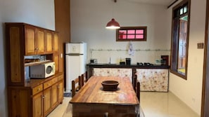 Una cocina con armarios de madera, microondas, mesa de comedor con sillas, lámpara colgante y ventana con vistas.
