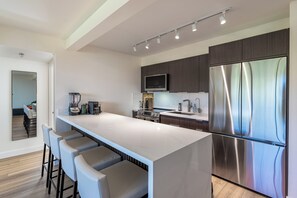 Cozinha moderna com geladeira de aço inoxidável, forno embutido e micro-ondas. Há banquetas no balcão e uma ilha grande.