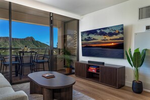A modern living room with a large flat-screen TV, a coffee table, and a sofa. - [New] Modern Luxe 2 Bedroom Condo in Waikiki with Diamond Head Views! (Honolulu)