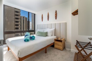 Habitación de hotel con una cama grande, una mesita de noche de madera, una ventana con vista a edificios y un perchero de toallas en la pared.