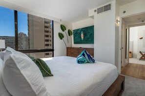 A hotel room with a large bed, a TV mounted on the wall, and a view of the cityscape through the window. - [New] Modern Luxe 2 Bedroom Condo in Waikiki with Diamond Head Views! (Honolulu)