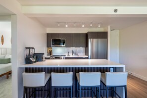 A modern kitchen with a central island, bar stools, a refrigerator, and a microwave. - [New] Modern Luxe 2 Bedroom Condo in Waikiki with Diamond Head Views! (Honolulu)