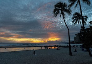 A beach with palm trees, a sunset, and people relaxing. - [New] Modern Luxe 2 Bedroom Condo in Waikiki with Diamond Head Views! (Honolulu)