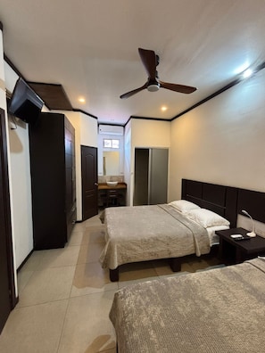 A hotel room with two beds, a ceiling fan, a TV, a bathroom, and a minibar.