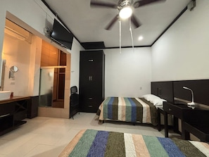 A bedroom with a bed, a desk, a chair, a wardrobe, and a ceiling fan.