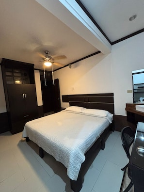 A bedroom with a bed, a desk, a chair, a wardrobe, and a ceiling fan.