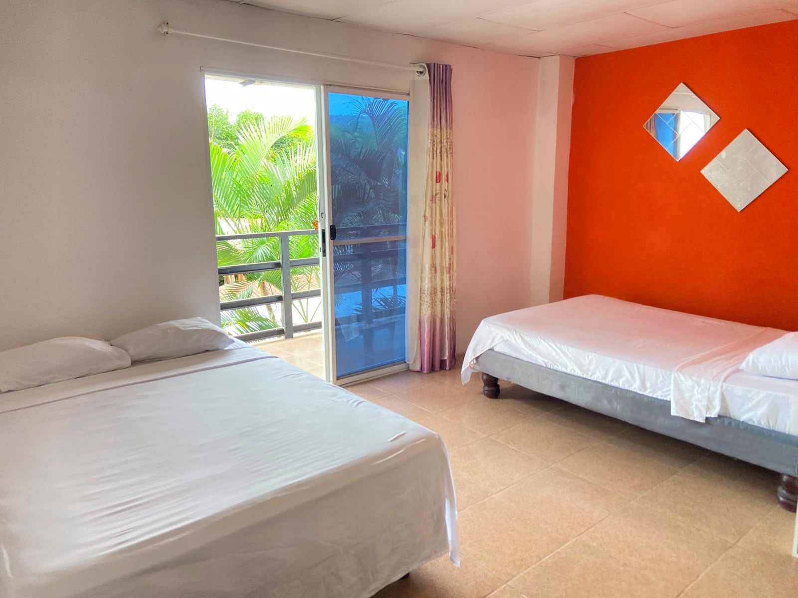Une chambre avec deux lits, une porte-fenêtre coulissante donnant sur un balcon et un mur orange orné de deux miroirs encadrés.