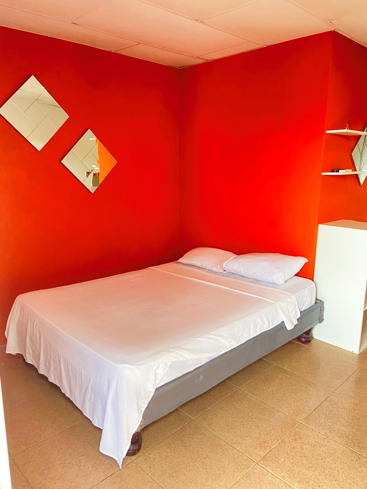 A single-bed room with a red wall, a white bed, and a white cabinet.