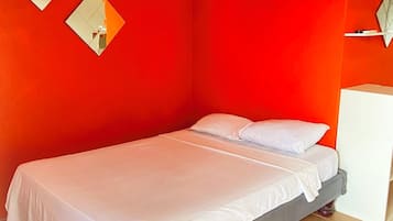 A single-bed room with a red wall, a white bed, and a white cabinet.