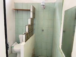 A bathroom with green tiles, a white toilet, and a shower area.