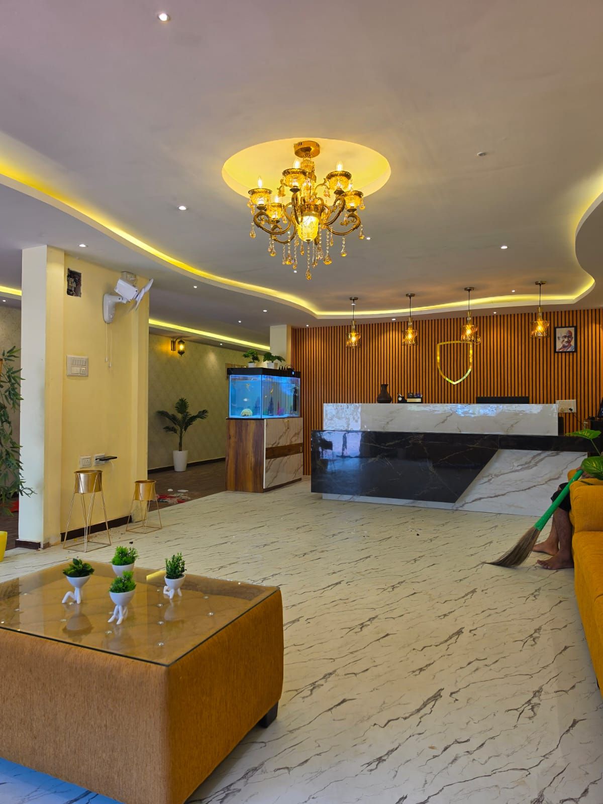 A hotel lobby with a reception desk, a chandelier, and a reception area with a television.