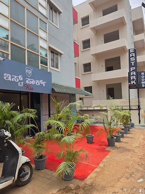 A hotel entrance with a red carpet, potted plants, and a parked scooter. - Hotel East Park Rio (Anekal)