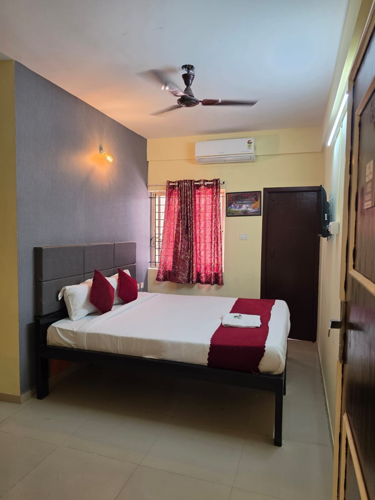 A bedroom with a bed, a ceiling fan, an air conditioning unit, and a door.