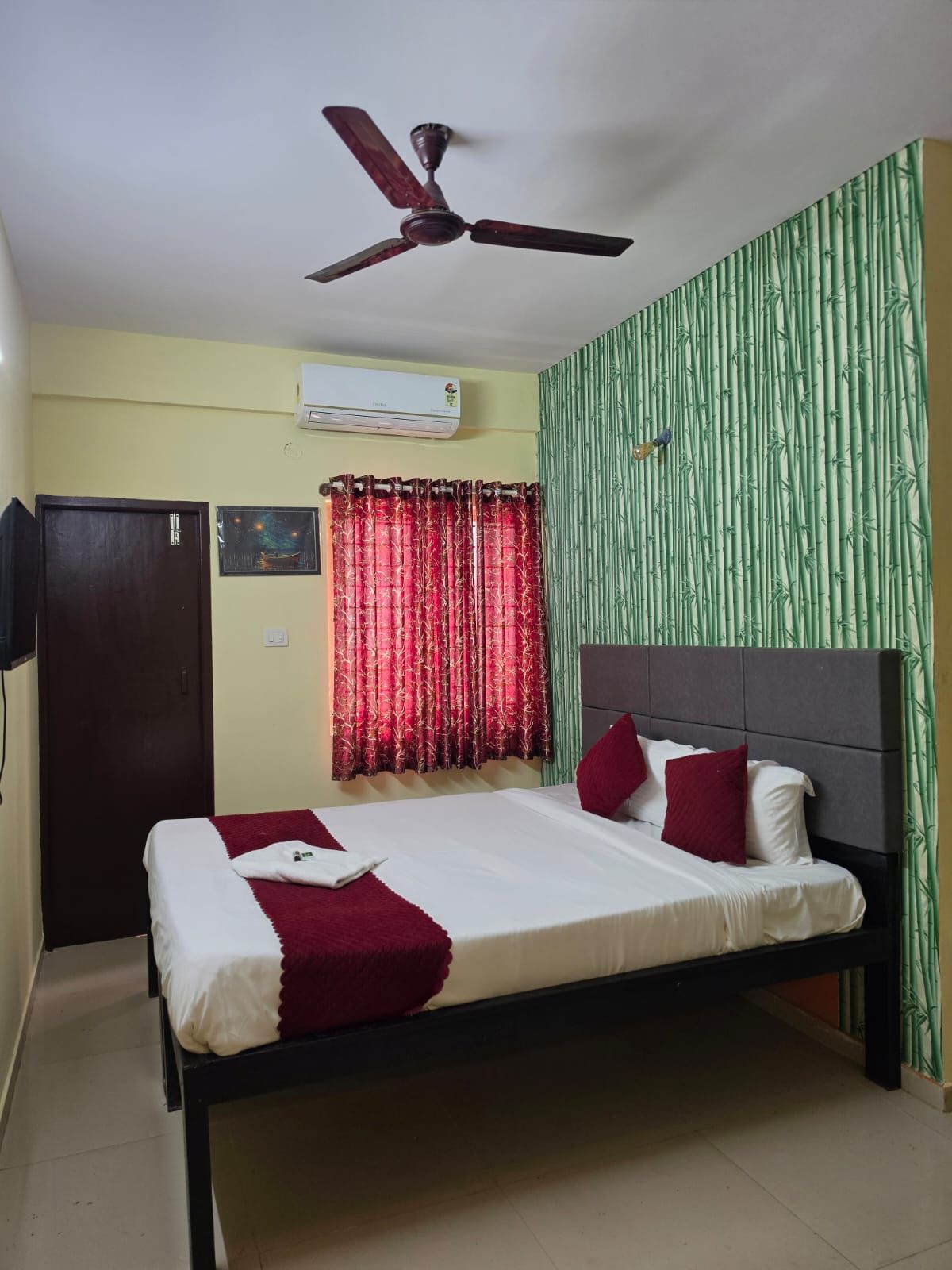 Habitación de hotel con cama, ventilador de techo, aire acondicionado, armario y pared con diseño de bambú vertical.