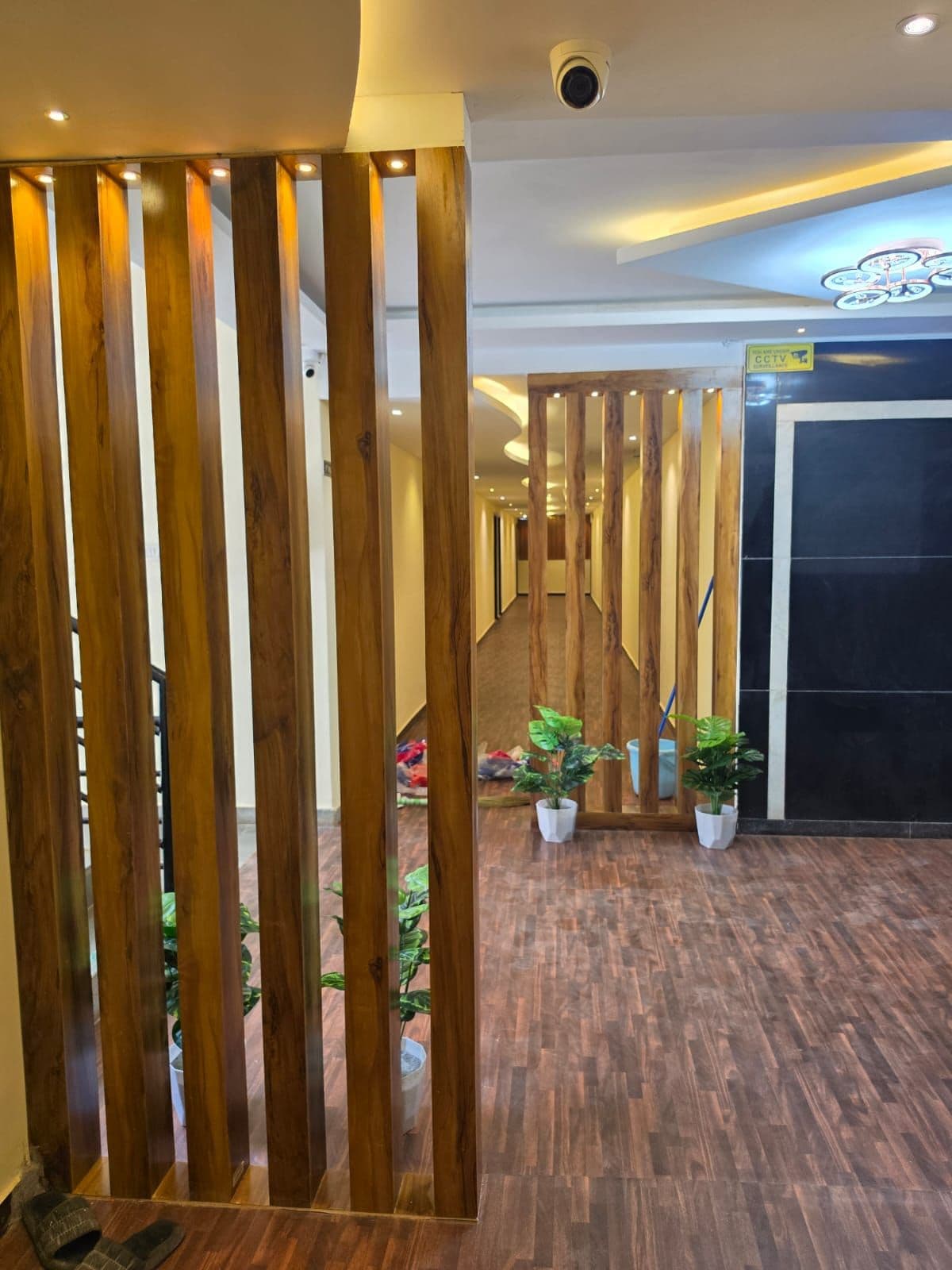 A hotel corridor with wooden partitions, potted plants, and a CCTV sign.