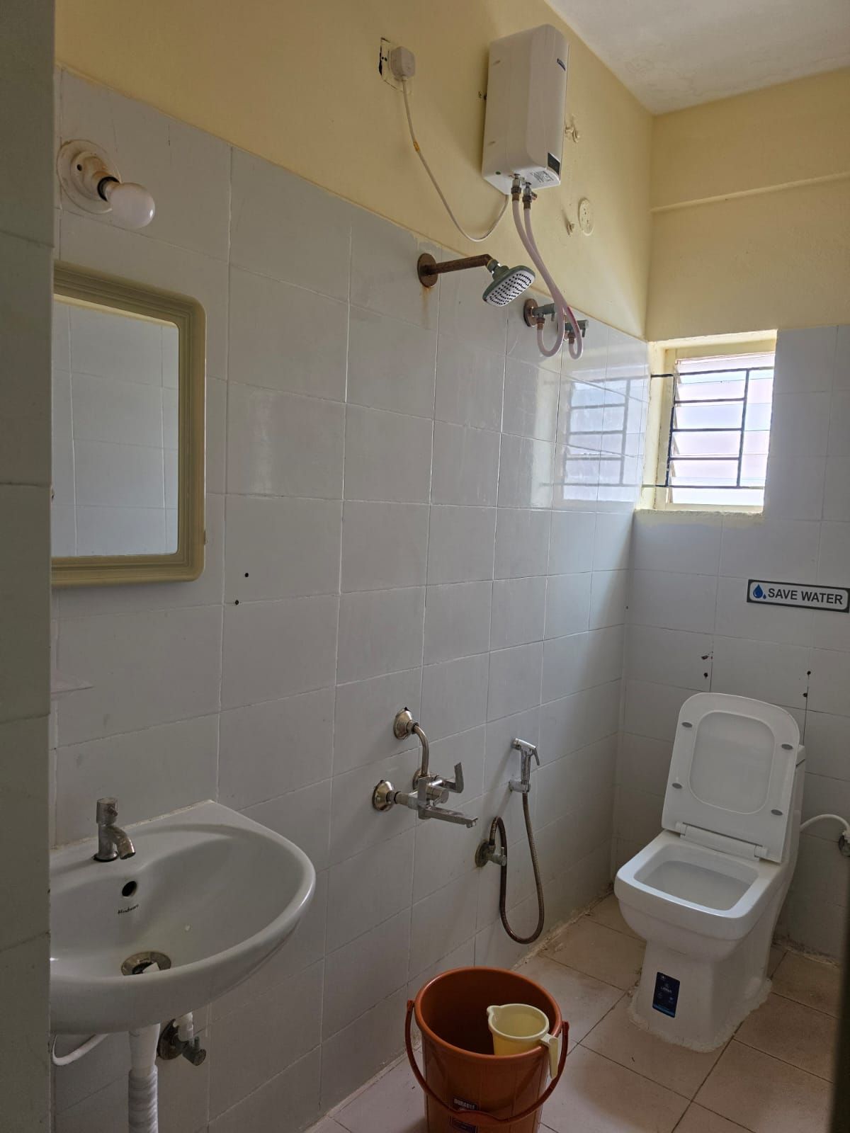 Un baño con lavamanos, inodoro, ducha y un balde.