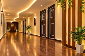 Un pasillo de hotel con suelo de madera, puertas oscuras y plantas en macetas.
