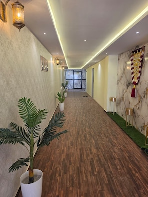 A hotel lobby with a wooden floor, potted plants, wall-mounted lights, and a marble wall with a decorative banner. - Hotel East Park Rio (Anekal)