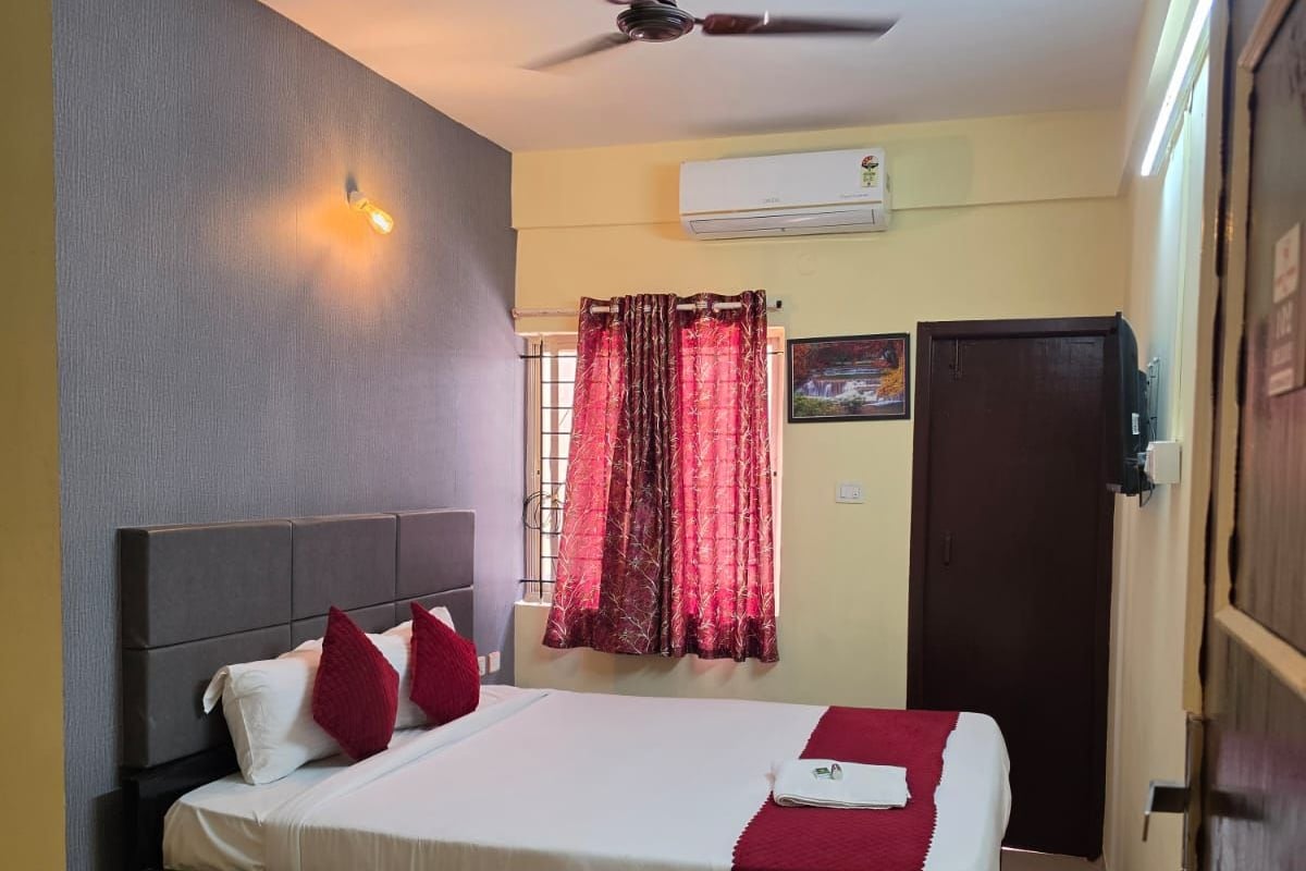 A bedroom with a bed, a ceiling fan, an air conditioning unit, and a door.