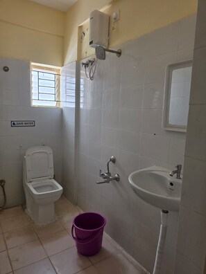 Un baño pequeño con inodoro, lavamanos y un cartel que dice 'AHORRA AGUA'.