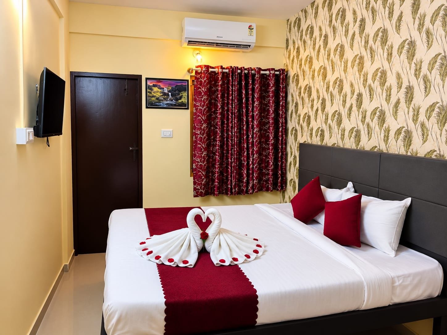 A hotel room with a bed, a television, an air conditioning unit, a door, and a wall with a floral wallpaper.