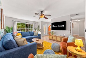 Ein modernes Wohnzimmer mit einem blauen Sofa, einem Holztisch und einem an der Wand befestigten Fernseher.
