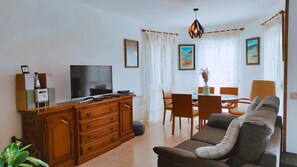 A living room with a television, wooden cabinet, sofa, dining table, chairs, and a plant. - Villa San Antonio with a private pool (Peníscola)