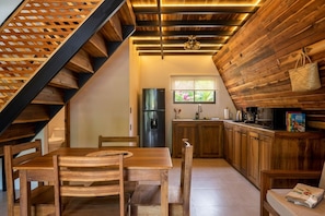 A kitchen with wooden cabinets, a refrigerator, and a window with a view of greenery. - SINA BUNGALOWS PUERTO VIEJO (Cahuita)