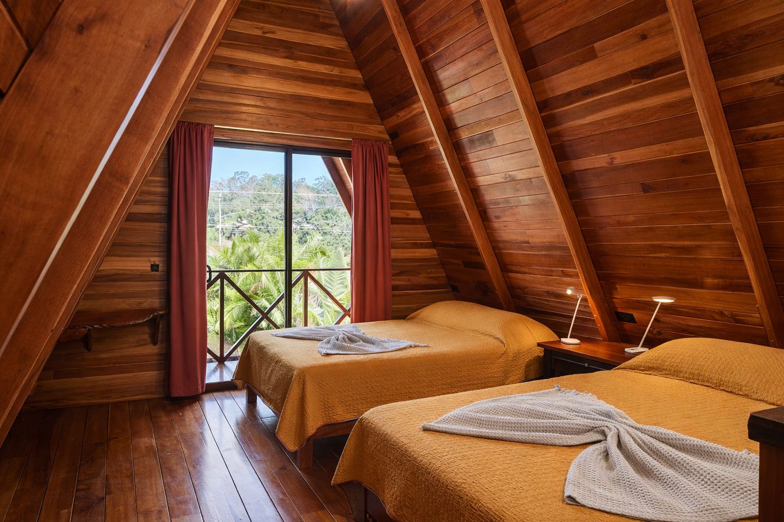 Una habitación con dos camas, vigas de madera en el techo, un balcón con cortinas y vistas al exterior con vegetación.