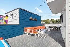 Ein Sitzbereich im Freien mit einem blauen Gebäude, einem weißen Sofa und einem Grill.