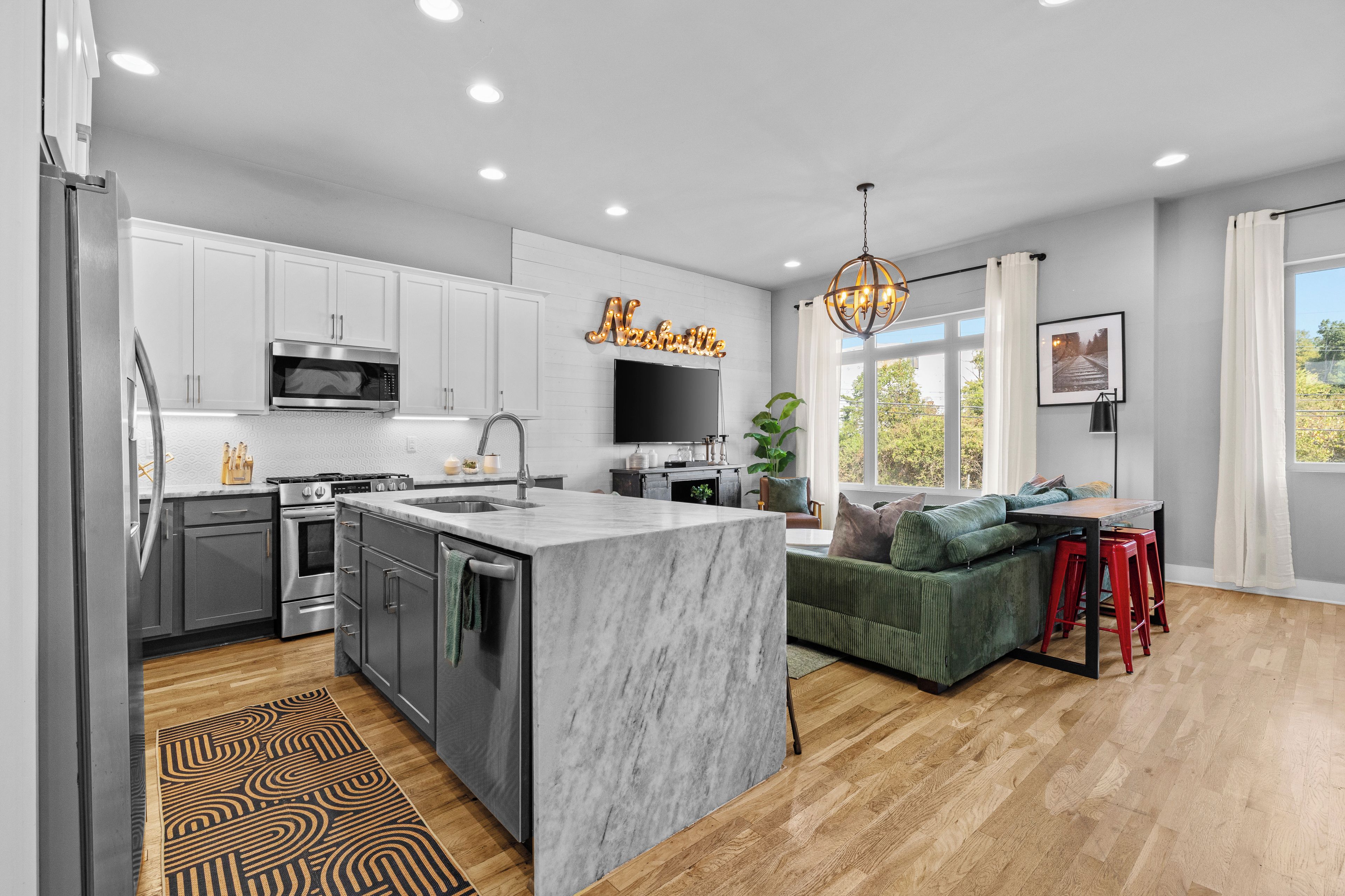 A modern kitchen with a marble island, stainless steel appliances, and a dining area with a green sofa and red stools.