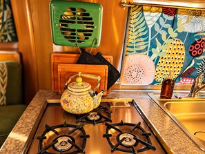 A kitchen with a gas stove, a decorative teapot, a green appliance, and a patterned wall. - Romantic Vintage Airstream Safari Near Puget Sound (Des Moines)