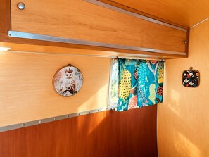 A compact interior with a wooden cabinet, a circular decorative item, a colorful curtain, and a small pouch. - Romantic Vintage Airstream Safari Near Puget Sound (Des Moines)