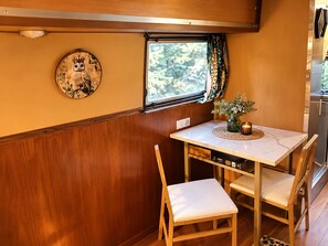 A compact kitchenette with a stainless steel refrigerator, a small dining table with two chairs, and a window with a view of greenery. - Romantic Vintage Airstream Safari Near Puget Sound (Des Moines)