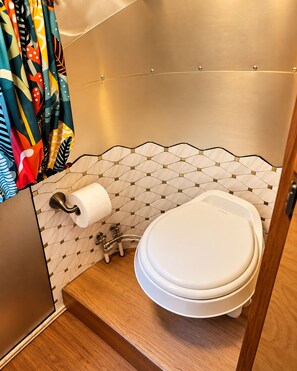 A compact bathroom with a toilet, a toilet paper holder, and a shower curtain. - Romantic Vintage Airstream Safari Near Puget Sound (Des Moines)