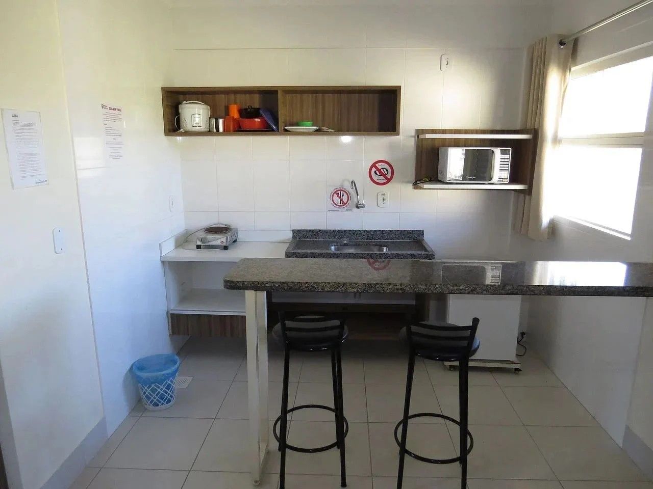 A compact kitchen with a granite countertop, two stools, a microwave, and a sink.