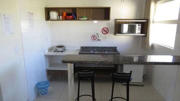 A compact kitchen with a granite countertop, two stools, a microwave, and a sink.