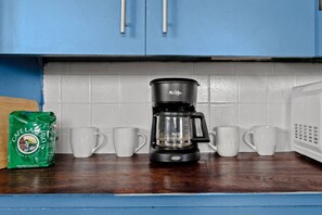Eine Kaffeemaschine auf einer Küchenarbeitsplatte mit einer Kaffeepackung und mehreren weißen Tassen.