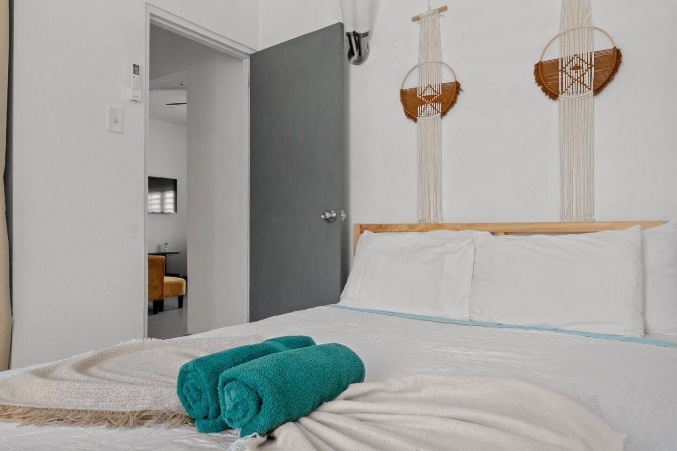 A hotel room with a bed, a door, a wall-mounted macrame decoration, and a view of a bathroom.