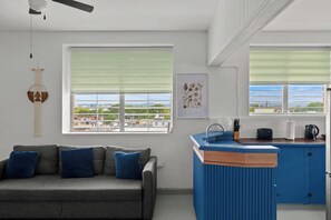 A modern kitchen with a blue countertop, a grey sofa with blue cushions, and a city view through the windows. - Santurce Blue 2BR | Near Beach & La Placita (San)