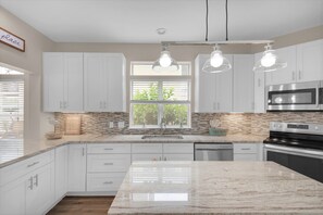 A modern kitchen with white cabinets, a marble countertop, and stainless steel appliances. - Sunkissed! Oceanview! Pool! Golf Cart! 6 Bedrooms (Destin)