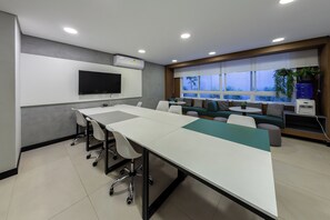 A conference room with a long table, chairs, a flat-screen TV, and a window with a view of greenery. - Guimarães by Bhomy (São Paulo)