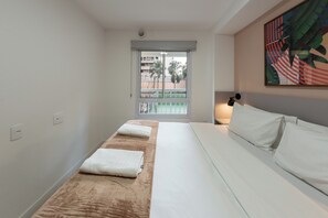 A hotel room with a bed, a window with a view of palm trees, a painting on the wall, and a bedside lamp. - Guimarães by Bhomy (São Paulo)