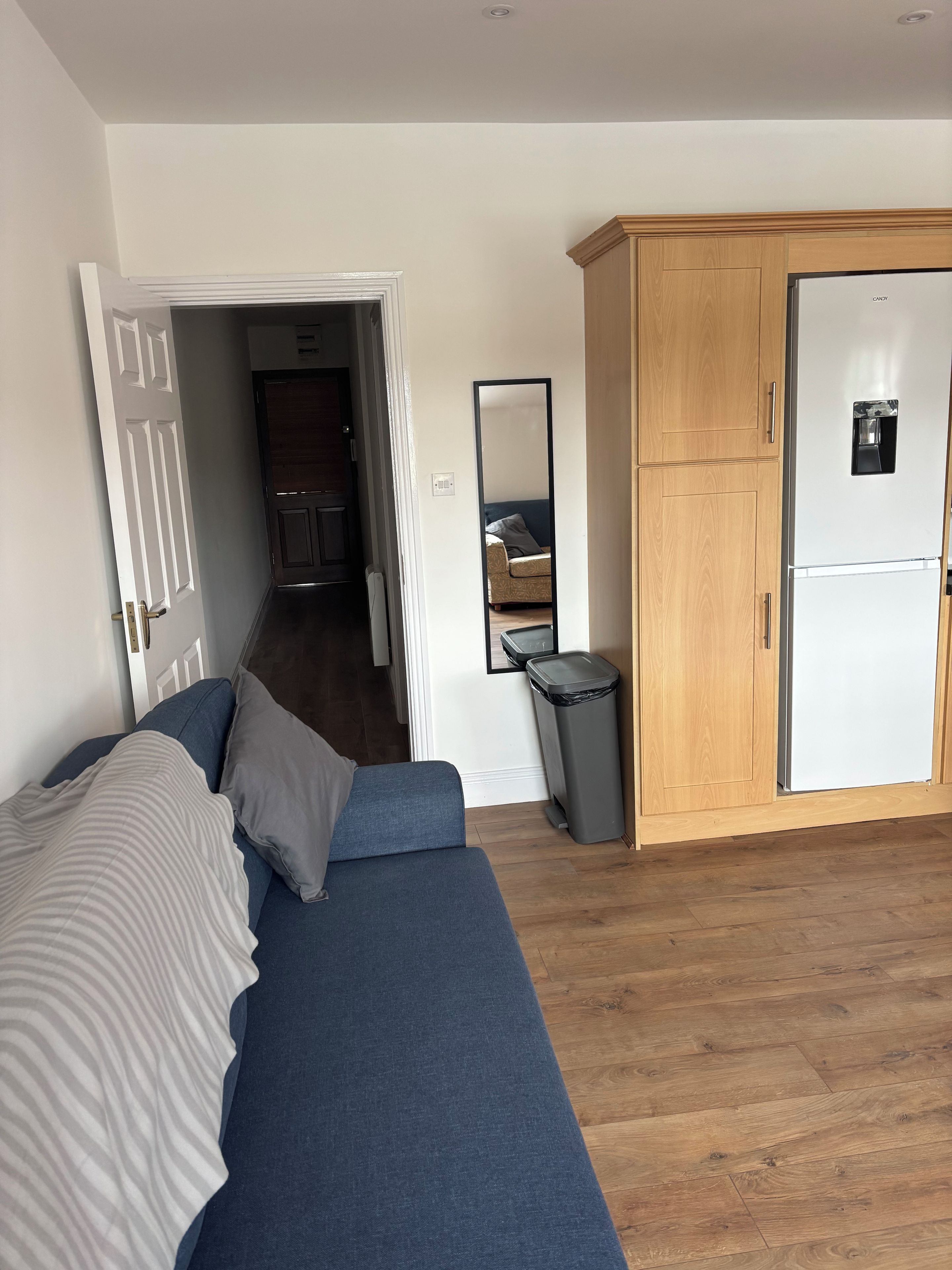 Ein Zimmer mit einem blauen Sofa, einem Holzschrank, einer weißen Tür und einem Spiegel.