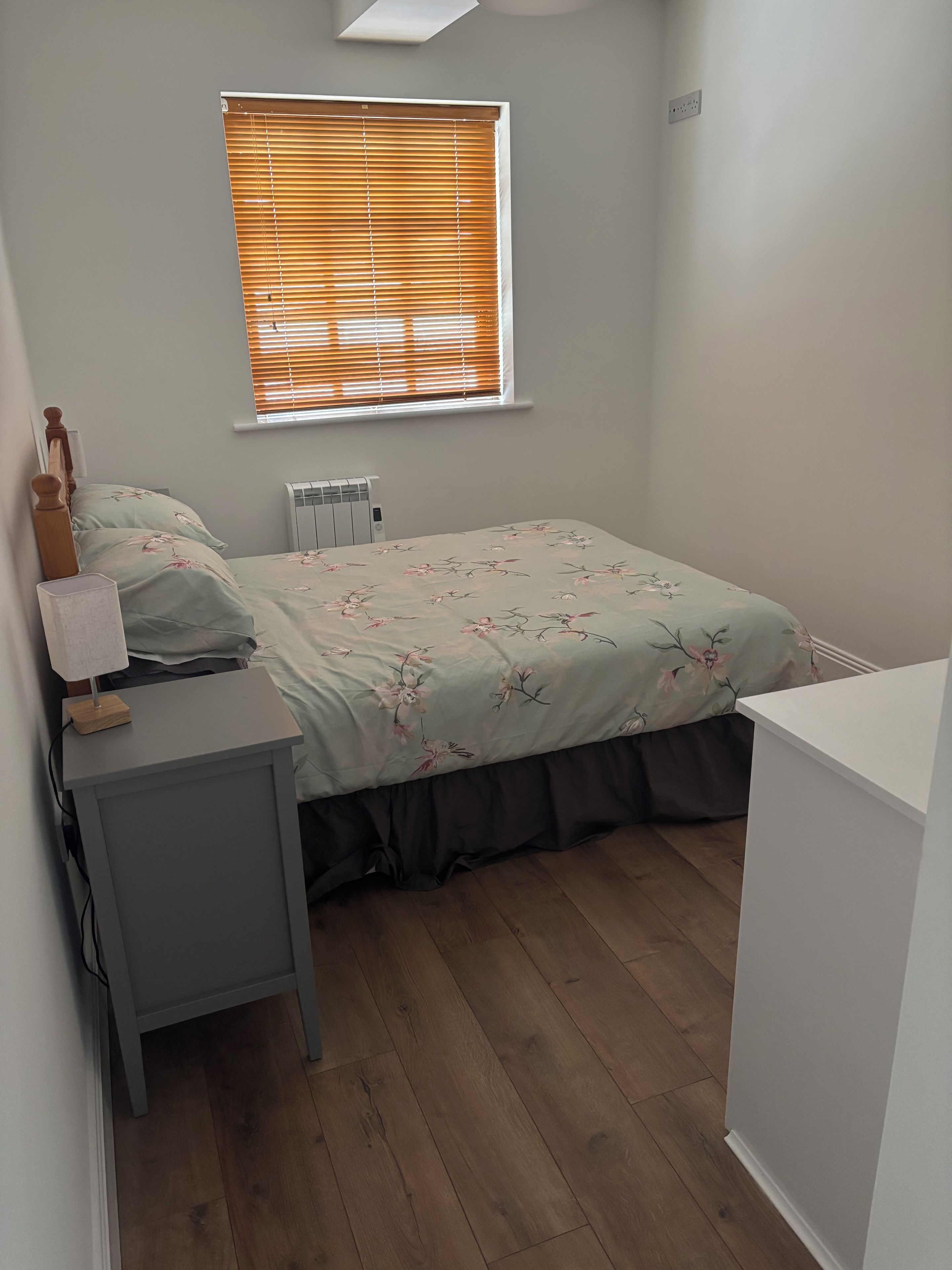 Une chambre à coucher avec un lit, une table de chevet avec une lampe, un radiateur et une fenêtre avec des stores.