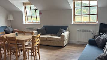 A room with a dining table, chairs, a sofa, and a television.