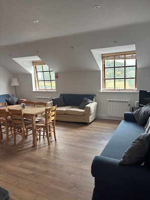 A room with a dining table, chairs, a sofa, and a television.