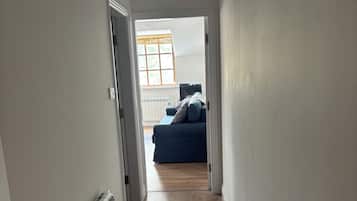A hallway with a radiator, a window with blinds, and a blue sofa in the distance.