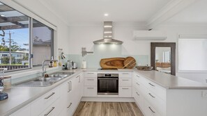 A modern kitchen with white cabinetry, stainless steel appliances, and a large window. - Shoreline Shack - Escape to the peaceful North Shore of Port Macquarie (North Shore)