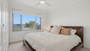 A bedroom with a large window, a bed with a headboard, and a ceiling fan. - Shoreline Shack - Escape to the peaceful North Shore of Port Macquarie (North Shore)